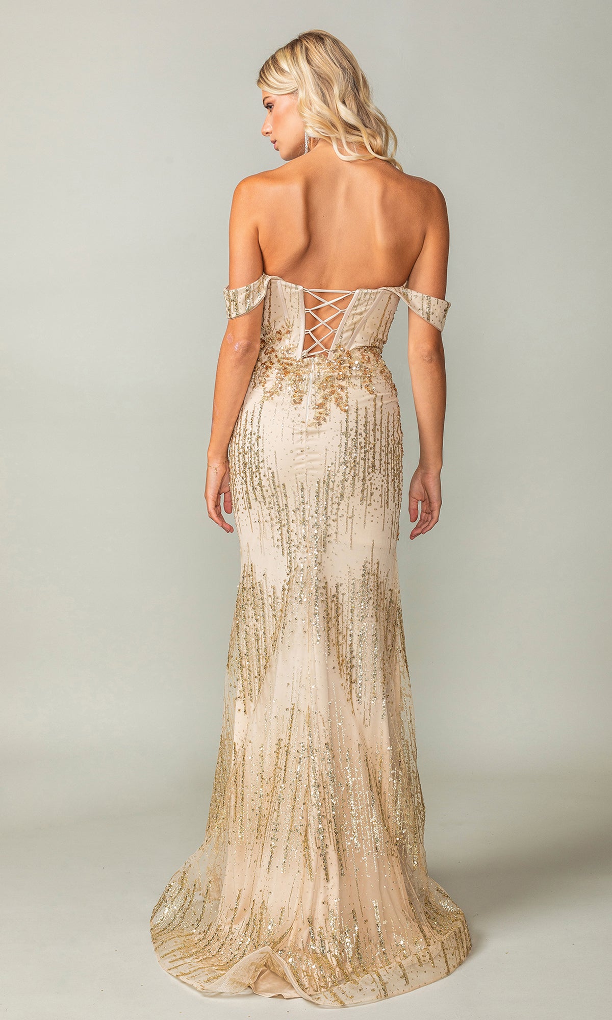 A woman faces away from the camera in the Off-the-Shoulder Long Sweetheart Prom Dress 4395, a floor-length gold sequin gown with a lace-up back, set against a plain background.
